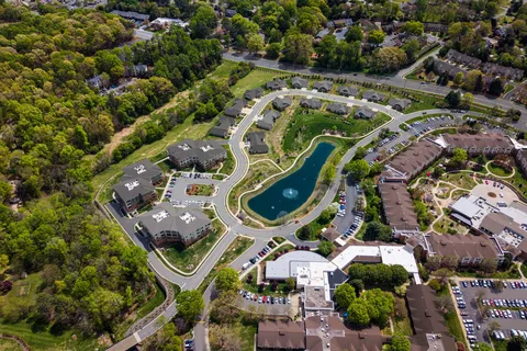 Aerial view of a managed apartment community with a fountain pond, lawns, and parking.