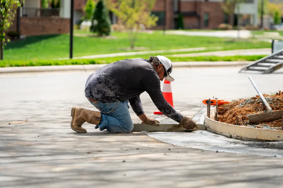 Crew member finishing the edge of a new curved concrete sidewalk.