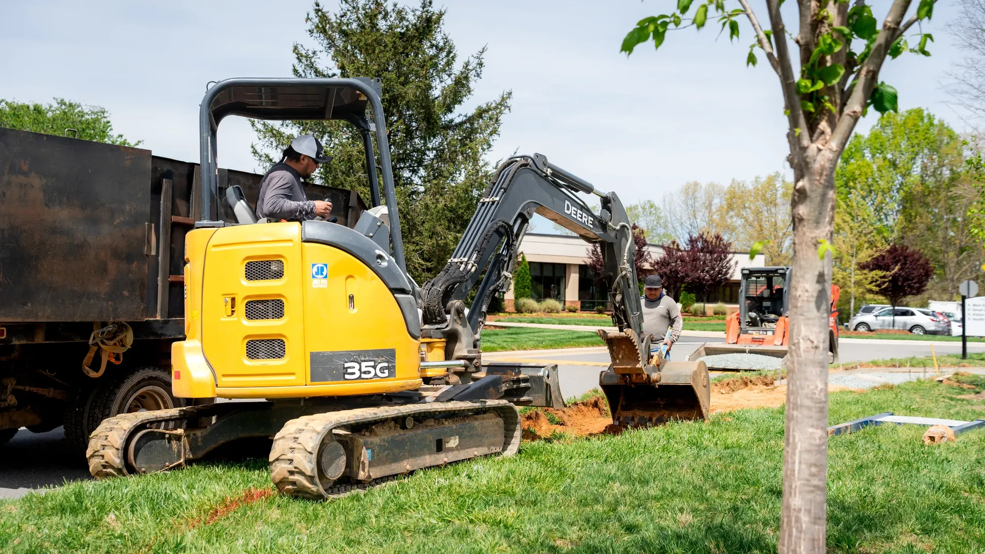 Crew using a compact excavator to dig a trench for a new sidewalk.