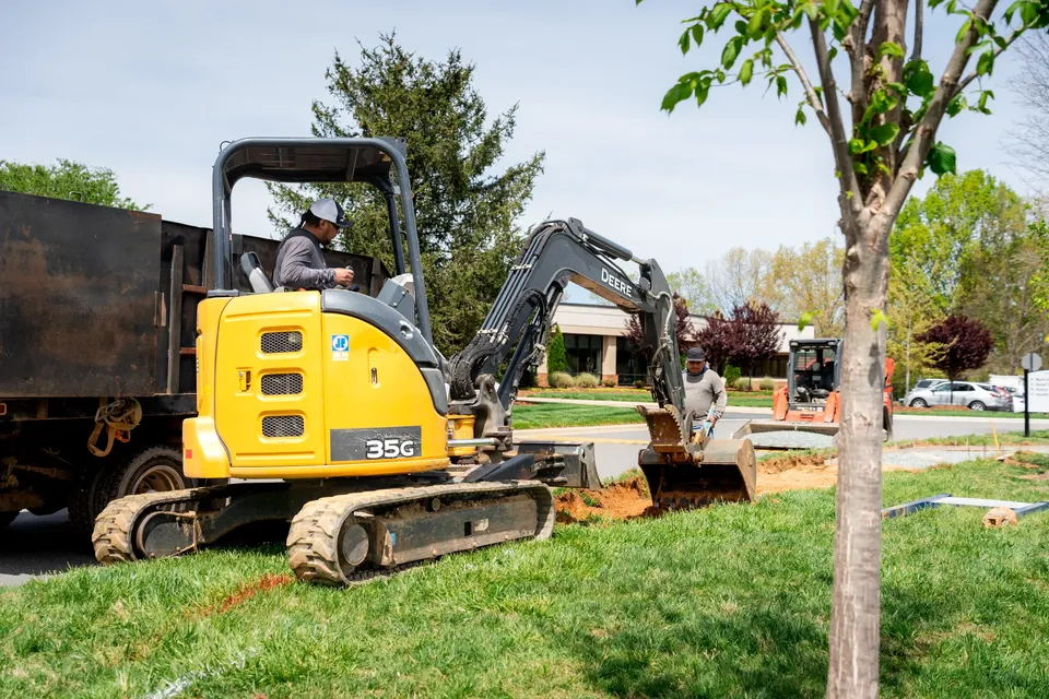 Crew using a compact excavator to dig a trench for a new sidewalk.