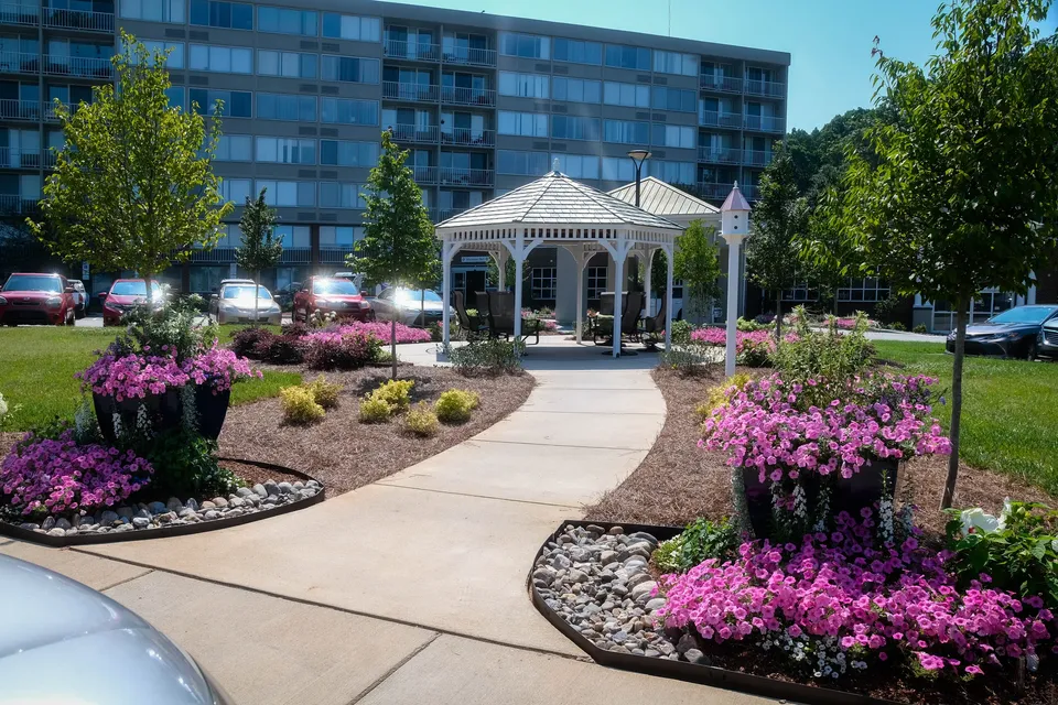Concrete walkway to a gazebo at an apartment community, lined with seasonal color.
